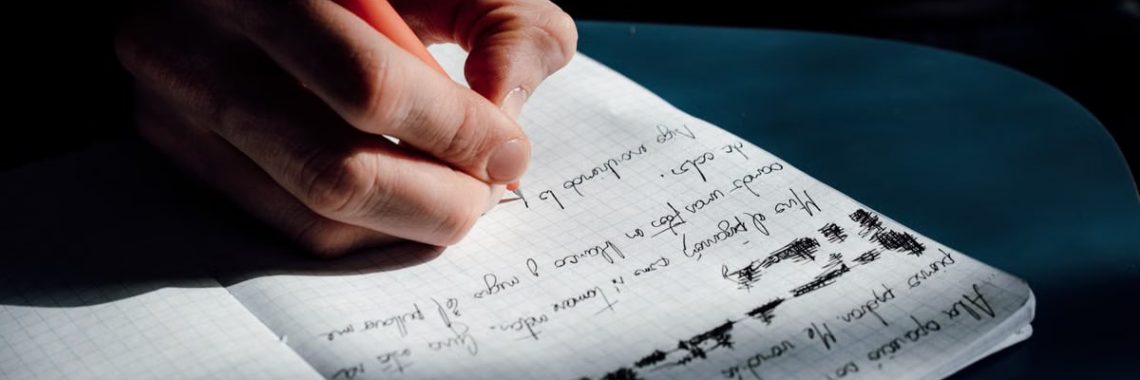 A person's hand writing in a notebook on a sunny day, showing detailed cursive notes.