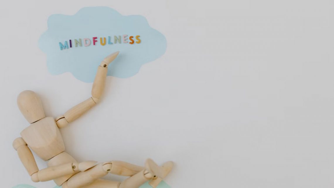 Wooden mannequin with mindfulness text on light blue cloud background, conveying calm.