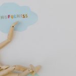 Wooden mannequin with mindfulness text on light blue cloud background, conveying calm.